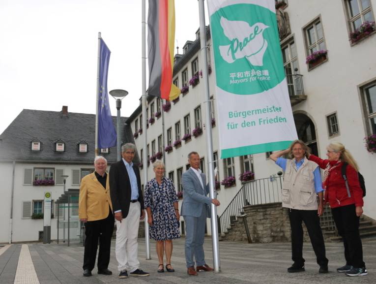Frauen und Männer mit der Mayors-for-Peace-Flagge vor dem Rathaus in Rüsselsheim.